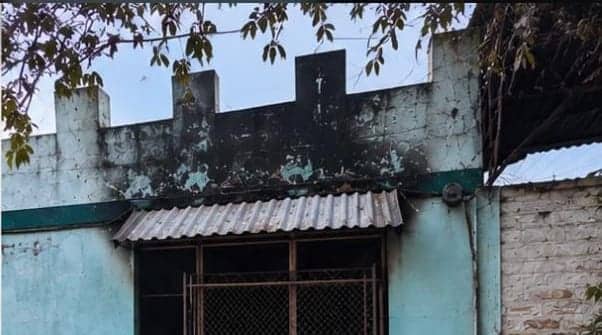 El frente de la casa de día. La pared verde agua está manchada de negro arriba de la ventana y la pintura se levantó por el calor. La chapa del alero está retorcida.