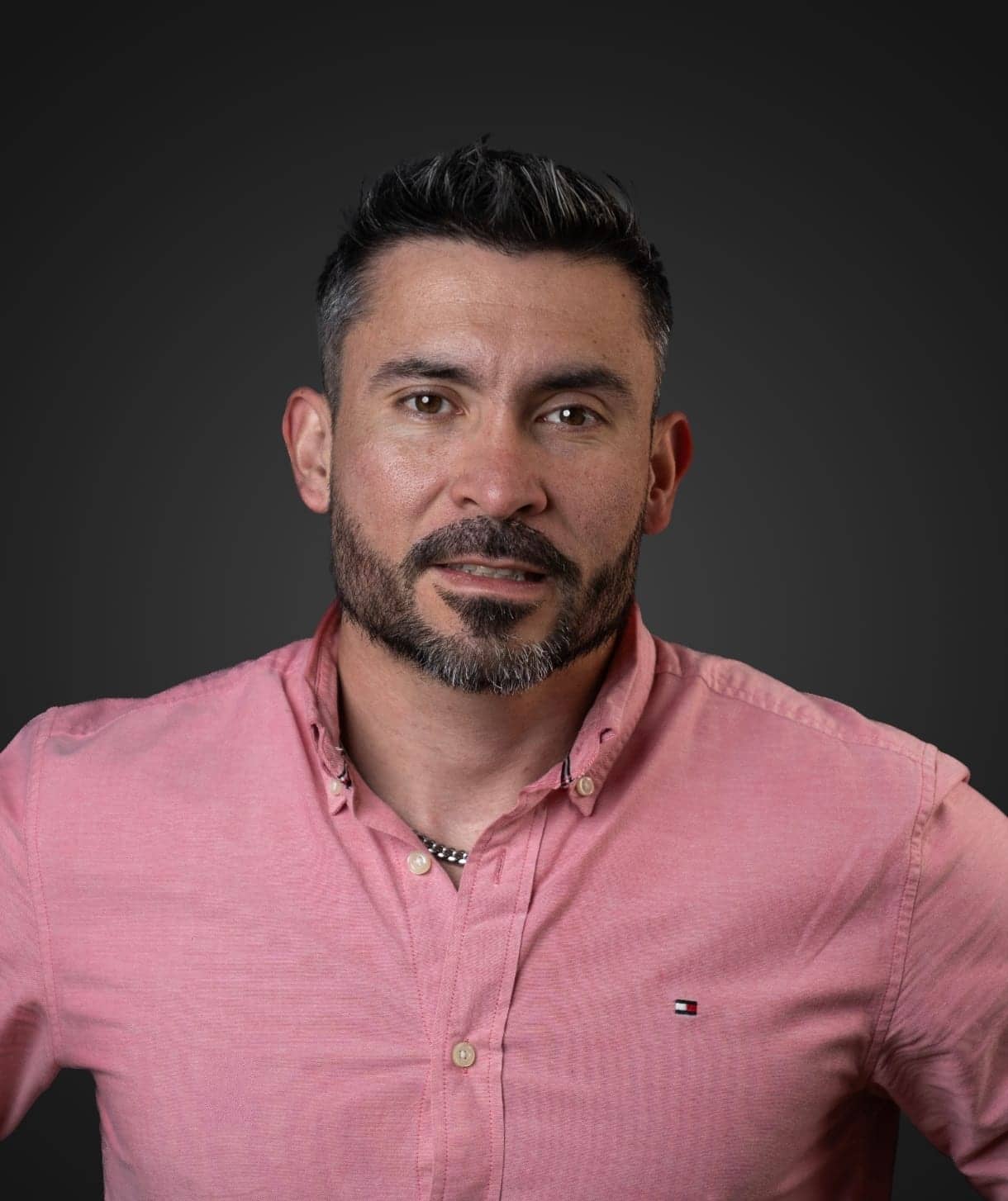 Portrait of Justo Miguel Vargas in a pink shirt, against a dark background.