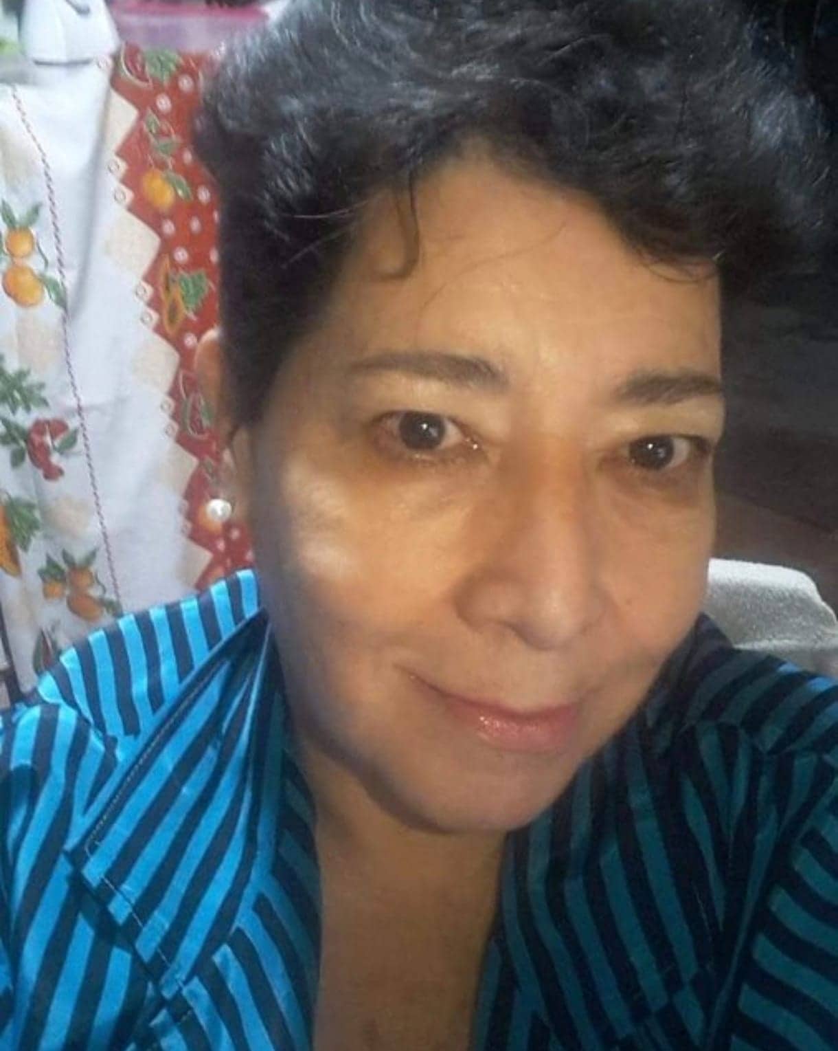 Retrato de Norma de cerca. Lleva una camisa a rayas celestes y azules y mira a la cámara con una sonrisa contenida.