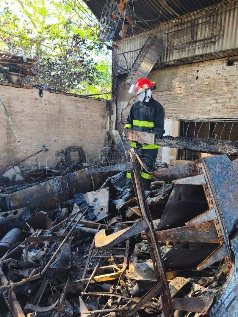 Un bombero de casco rojo entre hierros retorcidos, de día, en lo que quedó de la casa.